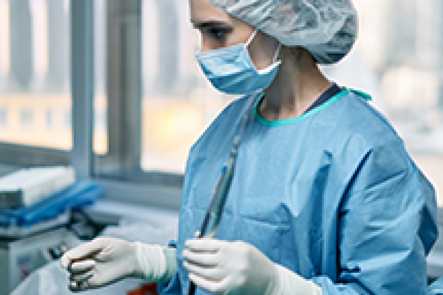 A dentist in full surgical scrubs holding a dental instrument.