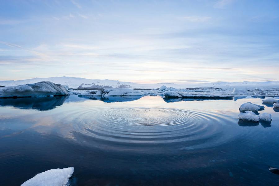A circular wave ripples through arctic water in the centre of a break in the sea ice.
